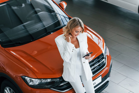 Leaning on the car. Woman in formal clothes is indoors in the autosalonの写真素材