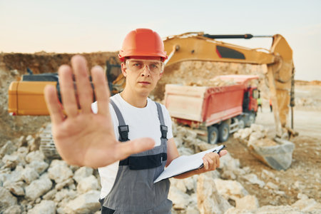 Showing stop sign by hand. Worker in professional uniform is on the borrow pit at daytimeの写真素材
