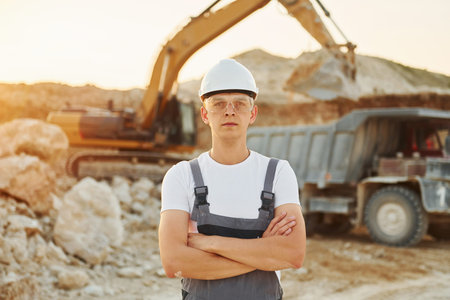 Standing with arms crossed. Worker in professional uniform is on the borrow pit at daytime