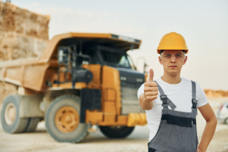 In glasses and hard hat. Worker in professional uniform is on the borrow pit at daytimeの写真素材