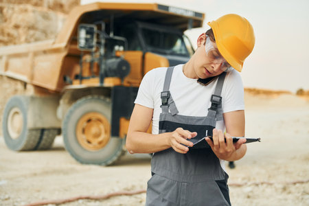 In glasses and hard hat. Worker in professional uniform is on the borrow pit at daytimeの写真素材