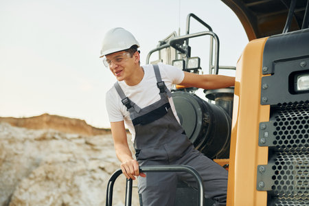 On the vehicle. Worker in professional uniform is on the borrow pit at daytimeの写真素材