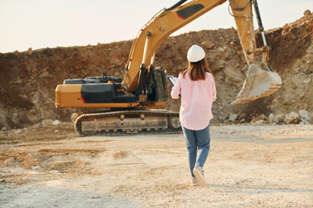 With documents. Young woman with documents in hard hat is standing on the borrow pitの写真素材