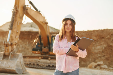 With documents. Young woman with documents in hard hat is standing on the borrow pitの写真素材