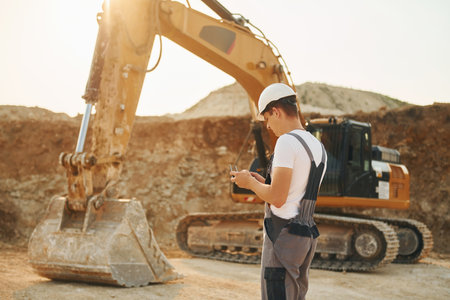 Illuminated by sunlight. Worker in professional uniform is on the borrow pit at daytimeの写真素材