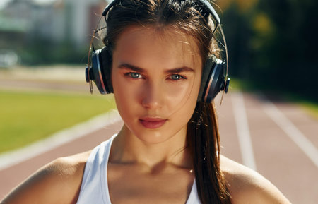 In headphones. Young woman in sportive clothes is exercising outdoorsの写真素材