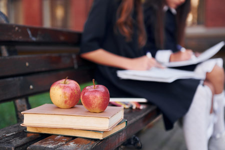 Apples is on the book. Two schoolgirls is outside together near school buildingの写真素材