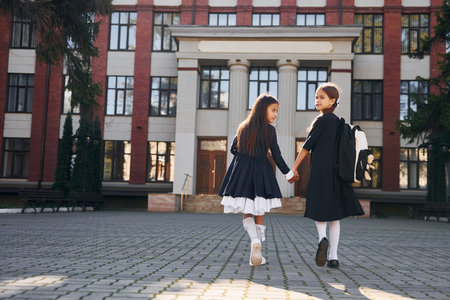 Rear view. Two schoolgirls is outside together near school buildingの写真素材