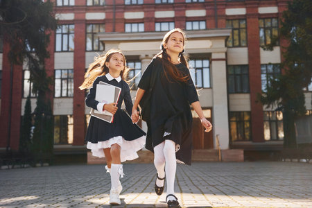 Two schoolgirls is running outside together near school buildingの写真素材