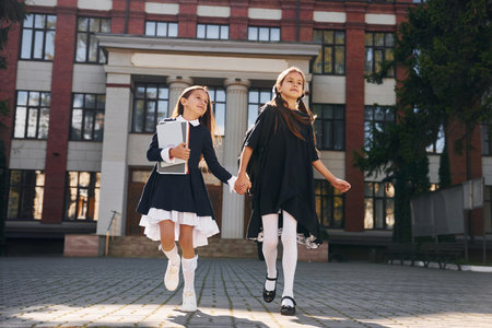 Two schoolgirls is running outside together near school buildingの写真素材