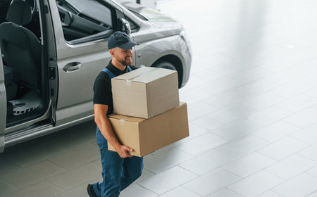 Business of service. Delivery man in uniform is indoors with car and with order.の写真素材