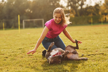 Playing on the ground. Woman in casual clothes is with pit bull outdoors.の写真素材