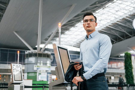 Standing by the terminal. Young businessman in formal clothes is in the airport at daytime.の写真素材
