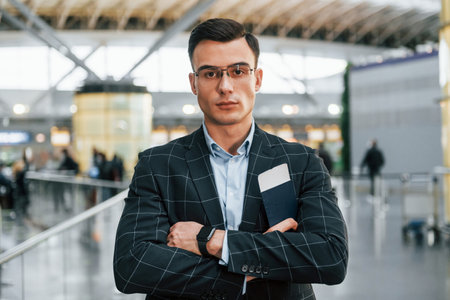 With arms crossed. Young businessman in formal clothes is in the airport at daytime.の写真素材