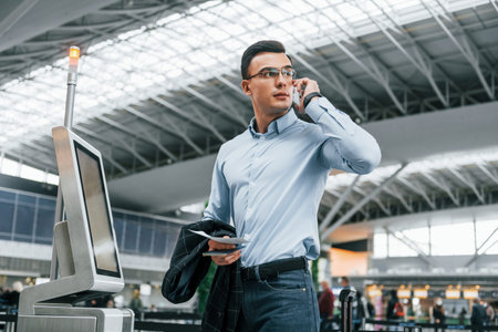 Holding phone. Young businessman in formal clothes is in the airport at daytime.の写真素材