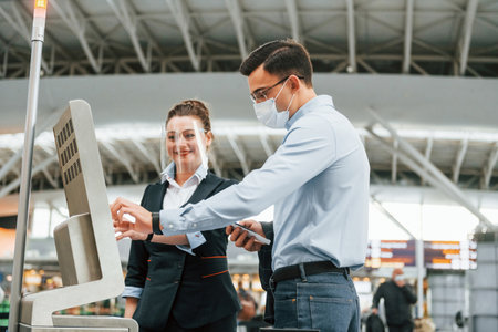 Employee helping using terminal. Young businessman in formal clothes is in the airport at daytime.の写真素材