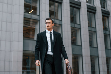 Conception of formal clothes. Businessman in black suit and tie is outdoors in the city.の写真素材