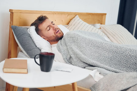 Sick man laying down on the bed at home and feels bad. Conception of self isolation.の写真素材