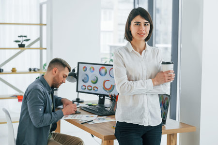 Woman standing in front of man that sitting by the table. Two designers working together in the...