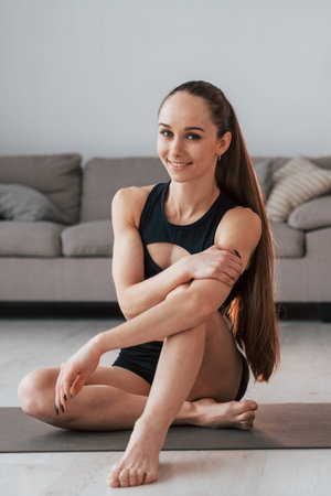 Sitting and smiling. Young woman with slim body type and in yoga clothes is at home.