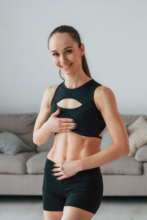 In black sportive clothes. Young woman with slim body type is at home.