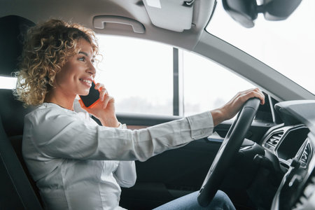 Using phone. Woman with curly blonde hair is in car.