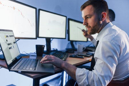 With laptop on the table. Two stock traders working in the office with exchange technology.