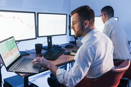 With laptop on the table. Two stock traders working in the office with exchange technology.