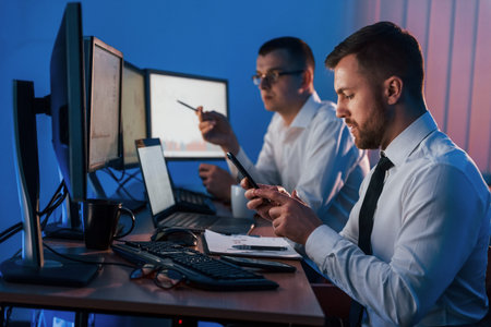 Holding smartphone in hands. Two stock traders working in the office with exchange technology.