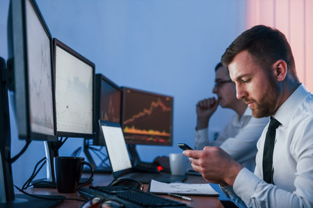 Holding smartphone in hands. Two stock traders working in the office with exchange technology.