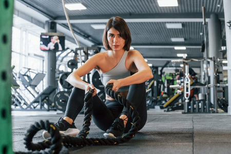 With special equipment. Woman in sportive clothes with slim body type is in the gym.