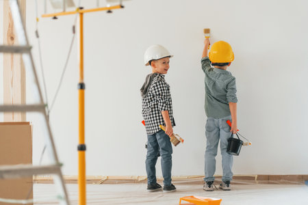Rear view. Two boys painting walls in the domestic room.の写真素材