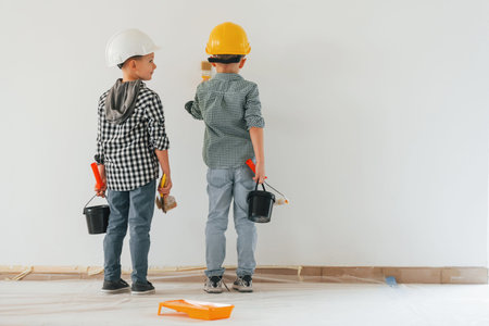 Rear view. Two boys painting walls in the domestic room.