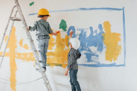 Two boys painting walls in the domestic room.