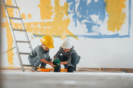 Friends together indoors. Two boys painting walls in the domestic room.