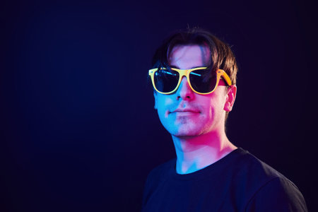 In yellow sunglasses. Man standing in the studio with neon light.の写真素材