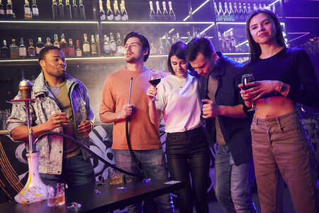 Standing near the table with hookah. Group of friends having fun in the night club together.