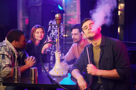 Sitting and smoking hookah. Group of friends having fun in the night club together.