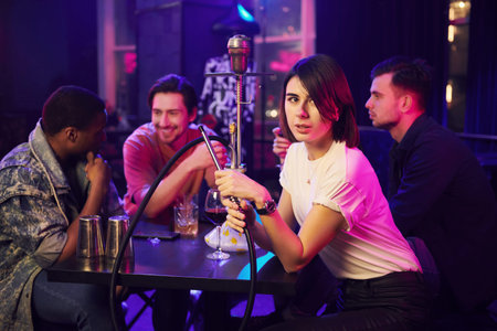Talking with each other when sitting by the table with hookah. Group of friends having fun in the...