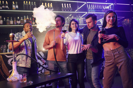 Standing near the table with hookah. Group of friends having fun in the night club together.