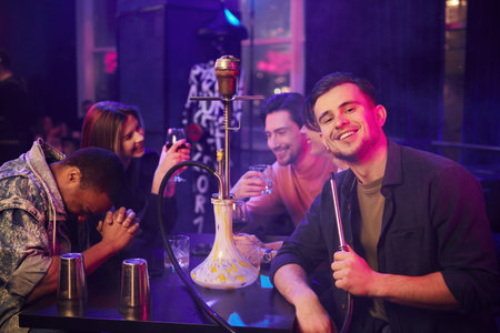 Sitting and smoking hookah. Group of friends having fun in the night club together.