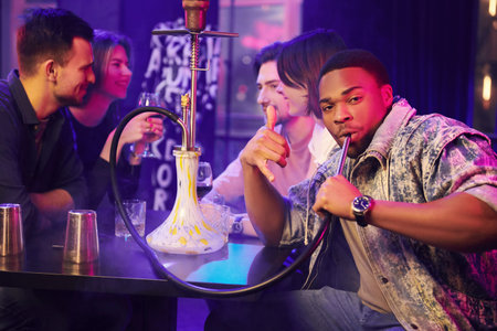 Sitting and smoking hookah. Group of friends having fun in the night club together.