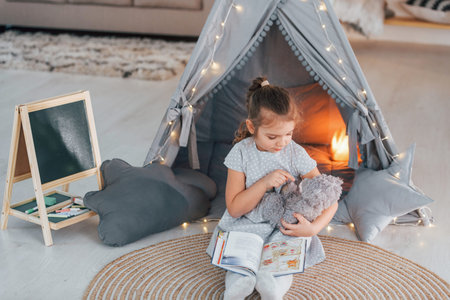At daytime. Cute little girl playing in the tent that is in the domestic room.