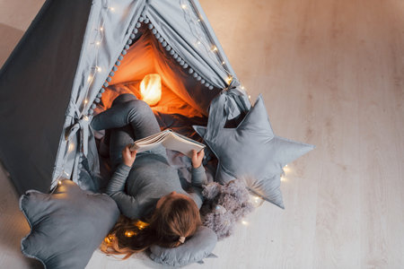 Interesting book. Cute little girl playing in the tent that is in the domestic room.の写真素材
