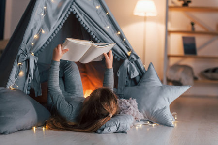Interesting book. Cute little girl playing in the tent that is in the domestic room.の写真素材