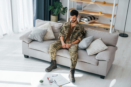 Bad mood. Post traumatic stress disorder. Soldier in uniform sitting indoors.の写真素材