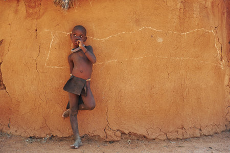 Namibia, Africa - June 14, 2021: Child of the ethnic people of Africa is outdoors. Standing against house.のeditorial素材