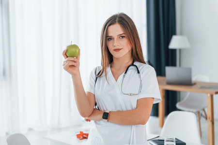Woman holding an apple. Professional medical worker in white coat is in the office.の写真素材