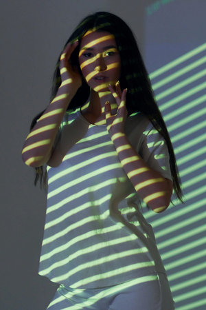 Green colored lines. Beautiful young woman is in projector neon lights in the studio.