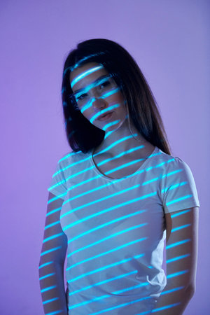 In eyewear in the lines. Beautiful young woman is in projector neon lights in the studio.